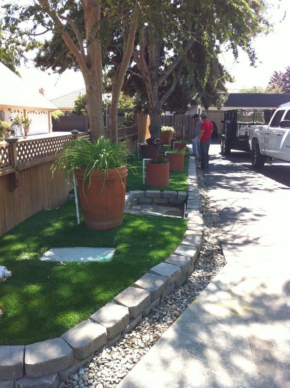 Sidewalk with potted plants and trees beside a parked white truck on a sunny day