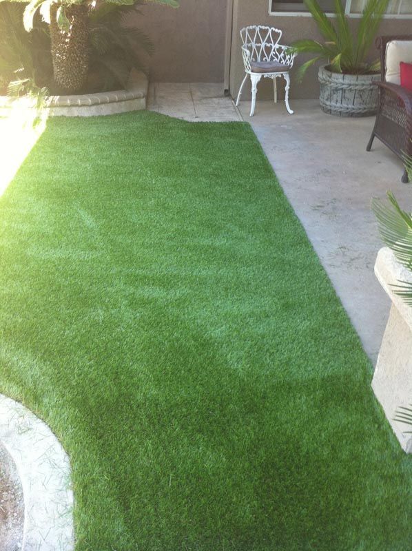 Small green artificial turf patch beside a patio with outdoor chairs and potted plants