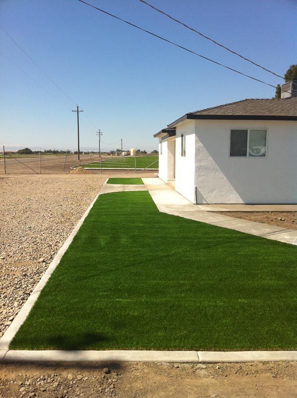 White house beside a bright green lawn and gravel yard under a clear blue sky