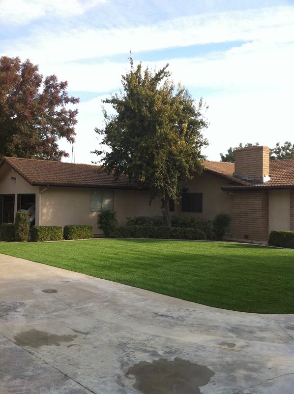 Single-story suburban house with a green lawn, driveway, trees, and a brick chimney under a clear sky