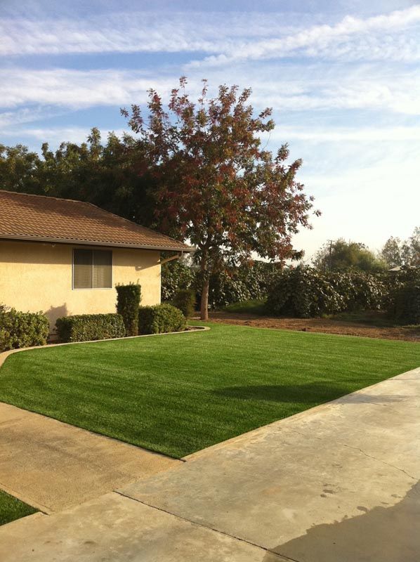 Suburban house with a green lawn, concrete driveway, and a tree under a partly cloudy sky