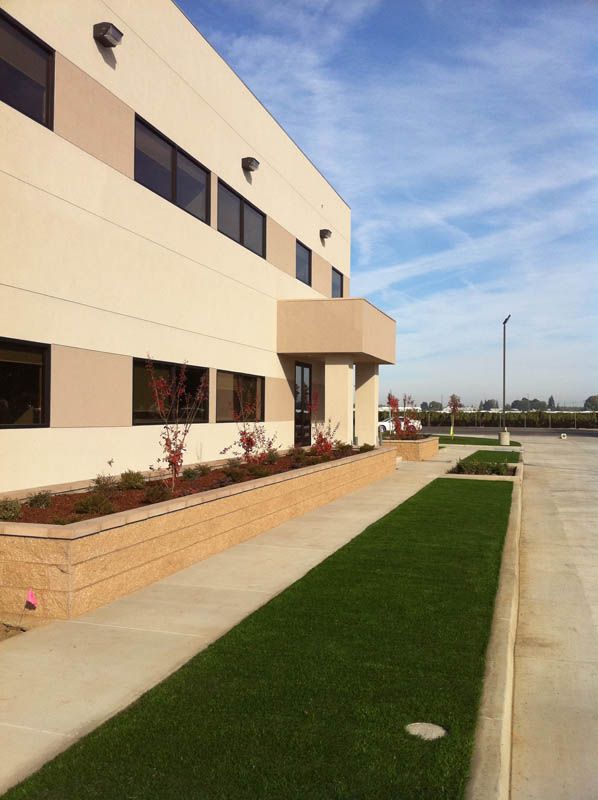 Modern beige building beside a green lawn and sidewalk under a blue sky