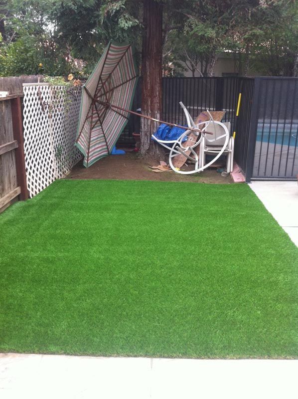 Small backyard with artificial grass, fence, trees, and a stacked bike and garden items at the back.