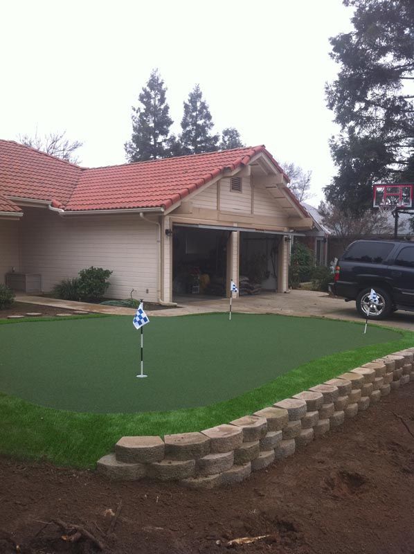 House with red-tile roof beside a small artificial putting green and a parked car