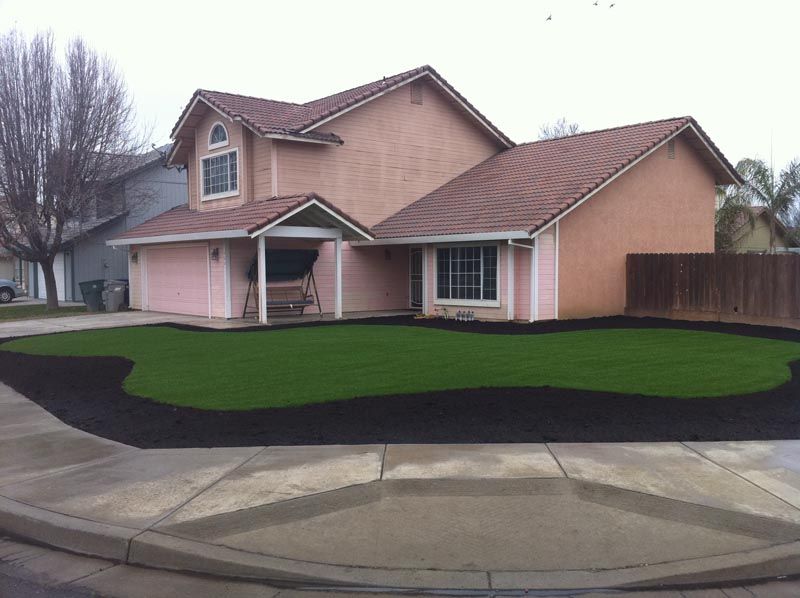Suburban two-story house with tan siding, green lawn, and curved black landscaping edging