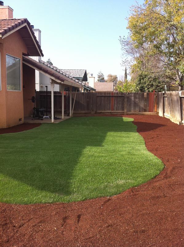 Backyard with green lawn and red mulch border beside a house and wooden fence
