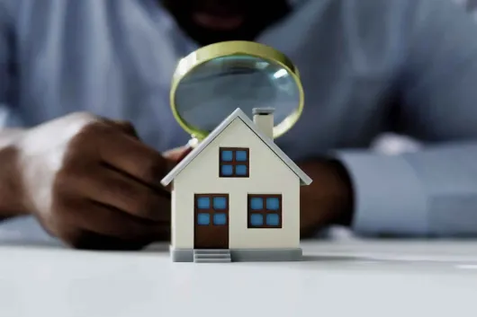 Magnifying glass inspecting a small house model on a table