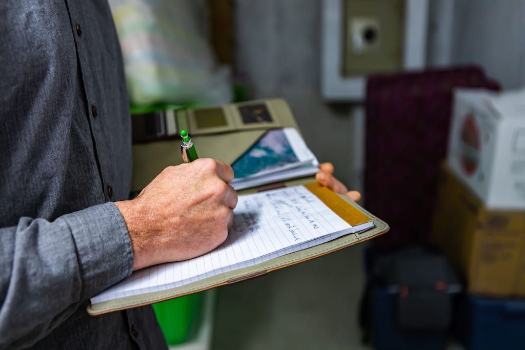 Person writing on a clipboard with a green pen in a room