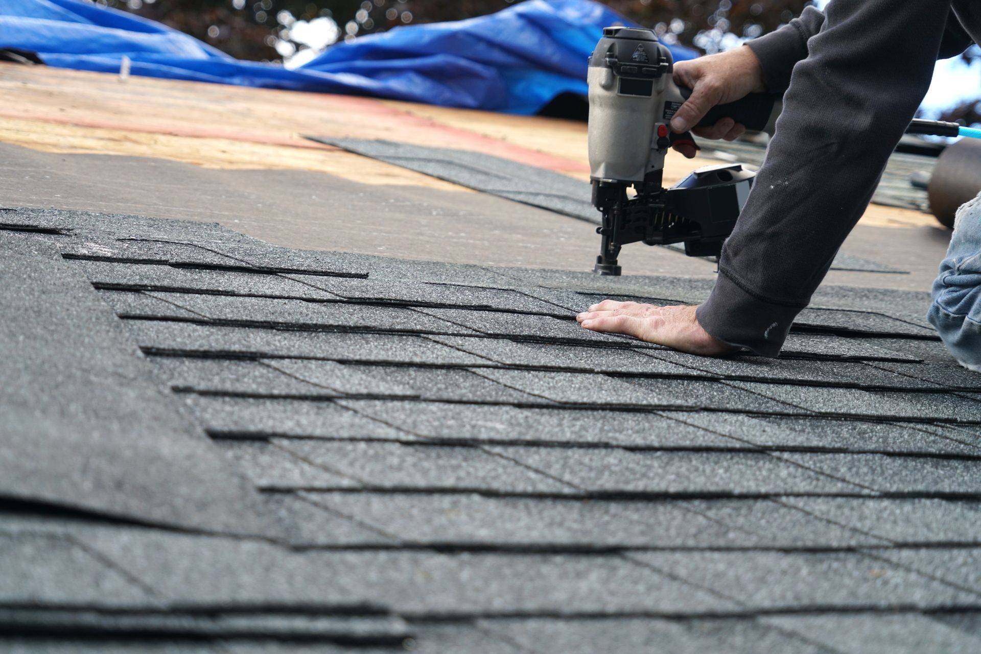 Worker installing roof shingles with a nail gun on a partially finished roof. Worker installing roof shingles with a nail gun on a partially finished roof.