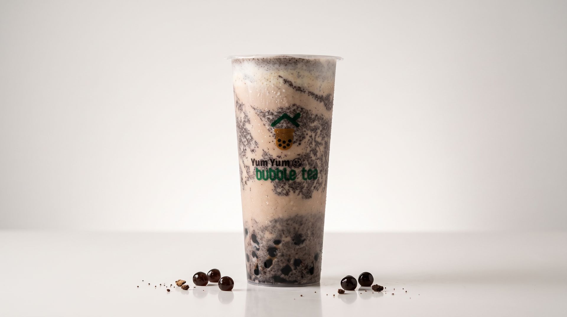 Tall clear cup with a layered iced drink, likely bubble tea, on a white surface with scattered pearls.