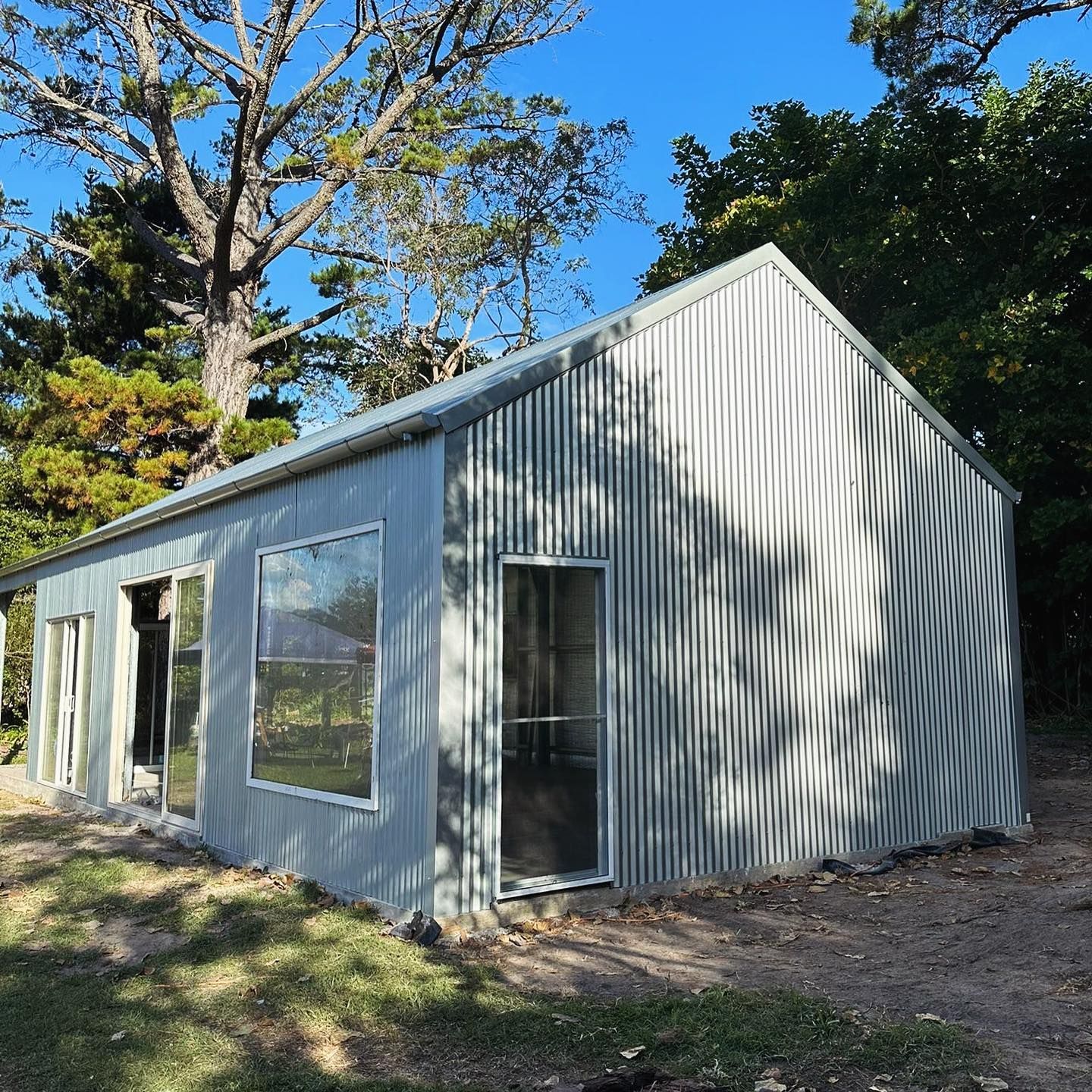 A Bike Parked Outside a Light Grey Shed with Open Doors, in A Backyard with Green Grass — Complete Sheds In Marulan, NSW