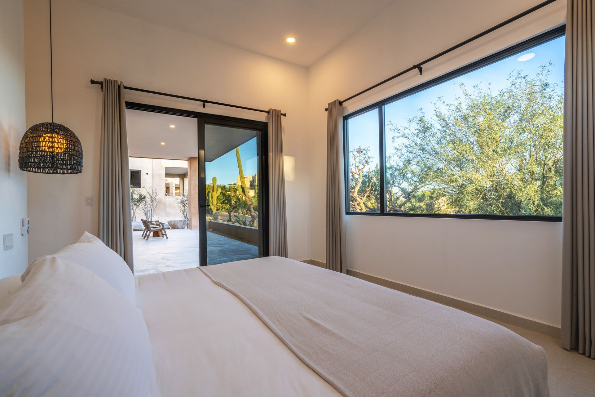 Bedroom with a large bed, sliding door to a patio, and a window with a view of greenery.