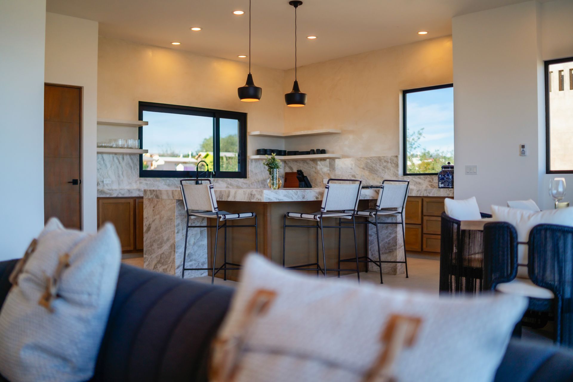 Modern kitchen with marble countertop, bar stools, and two black pendant lights.