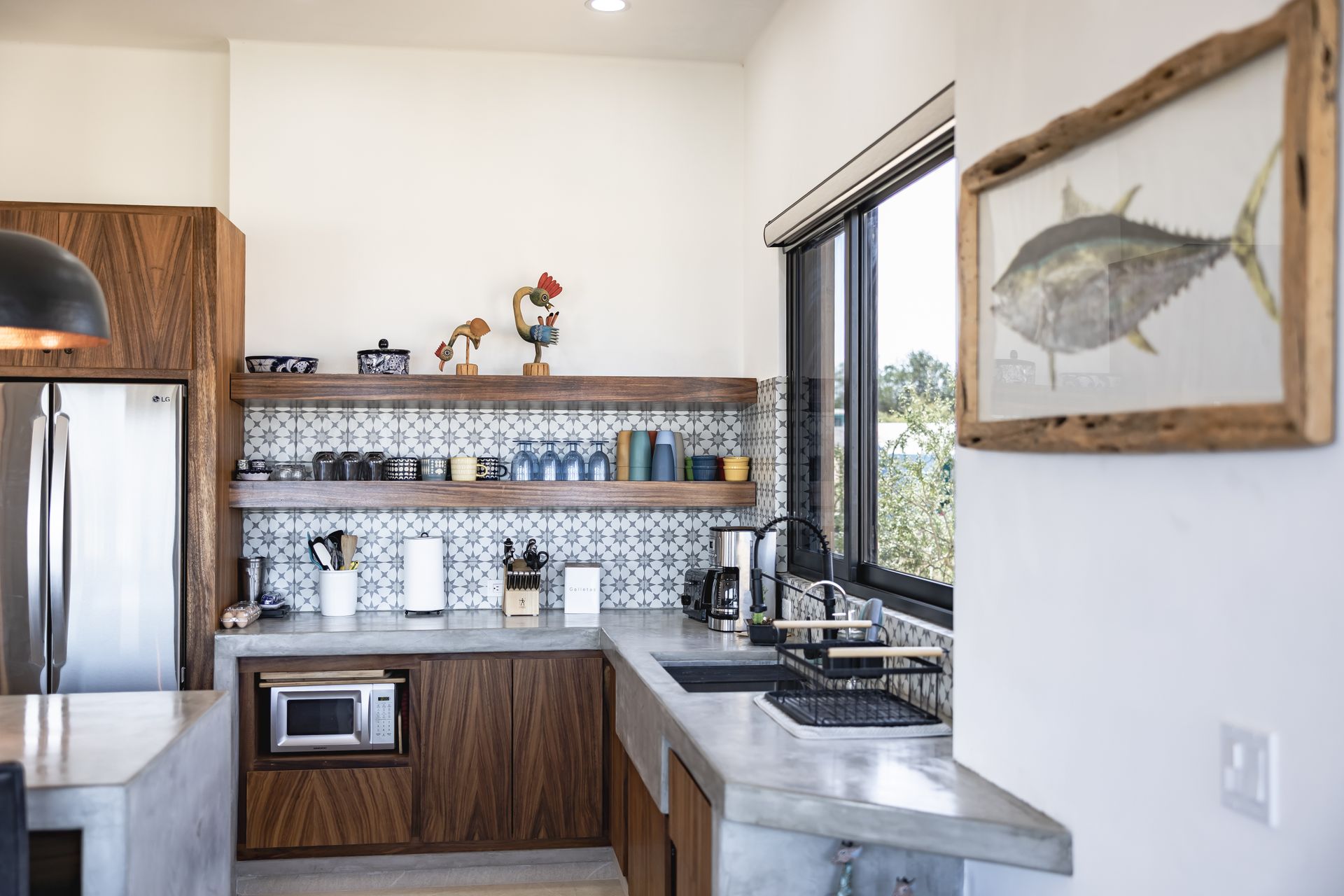 Kitchen with wood cabinets, concrete countertops, patterned backsplash, and window with fish art.