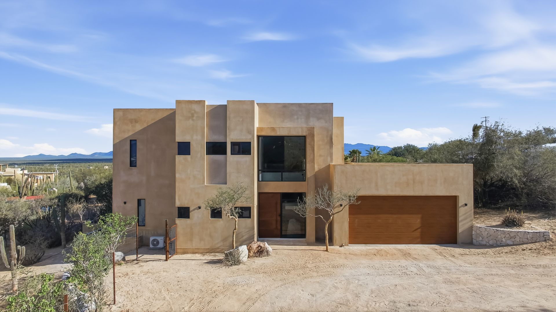 Modern two-story beige house with a wooden garage door on a sunny day.