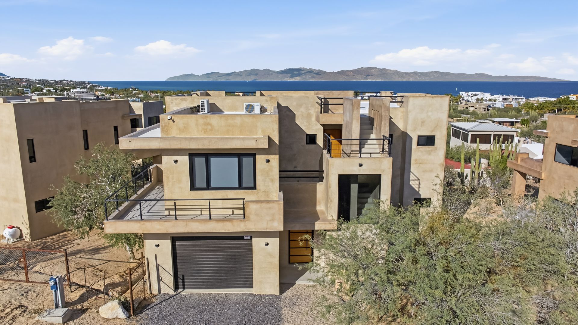 Two-story beige stucco house with ocean view and black garage door. Partially completed construction.