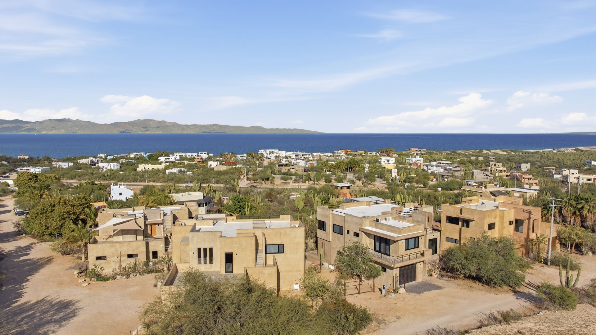 Overview of a coastal town with buildings and a body of water in the background under a blue sky.
