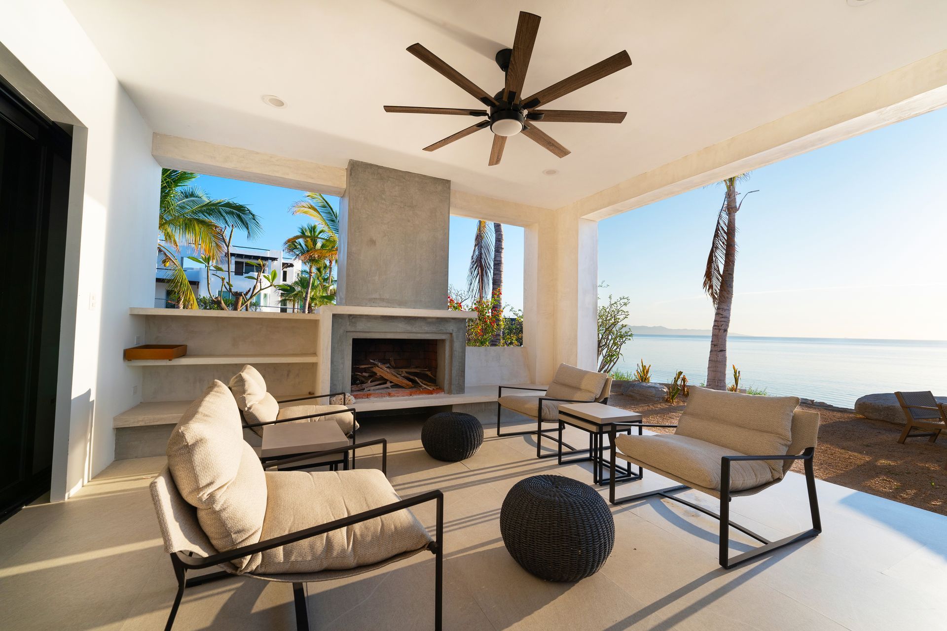Covered patio with seating, fireplace, ocean view, and ceiling fan.