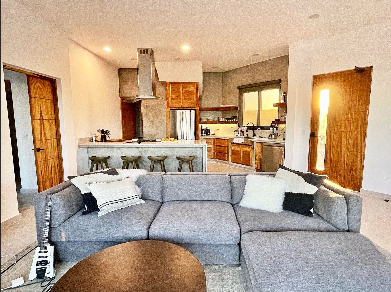 Spacious living area with a gray sectional sofa, kitchen with wooden cabinets, and sunset view.