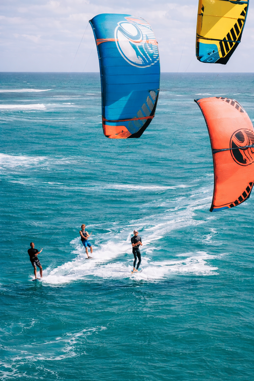 Kite surfers on ocean with colorful kites overhead.