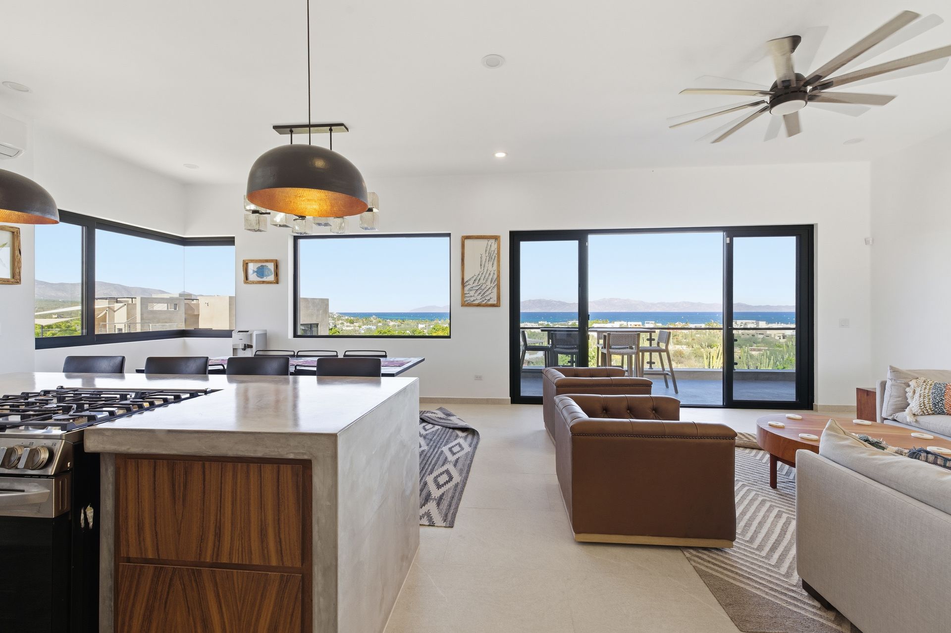 Modern open-plan living space with kitchen, seating area, large windows, and outdoor view.