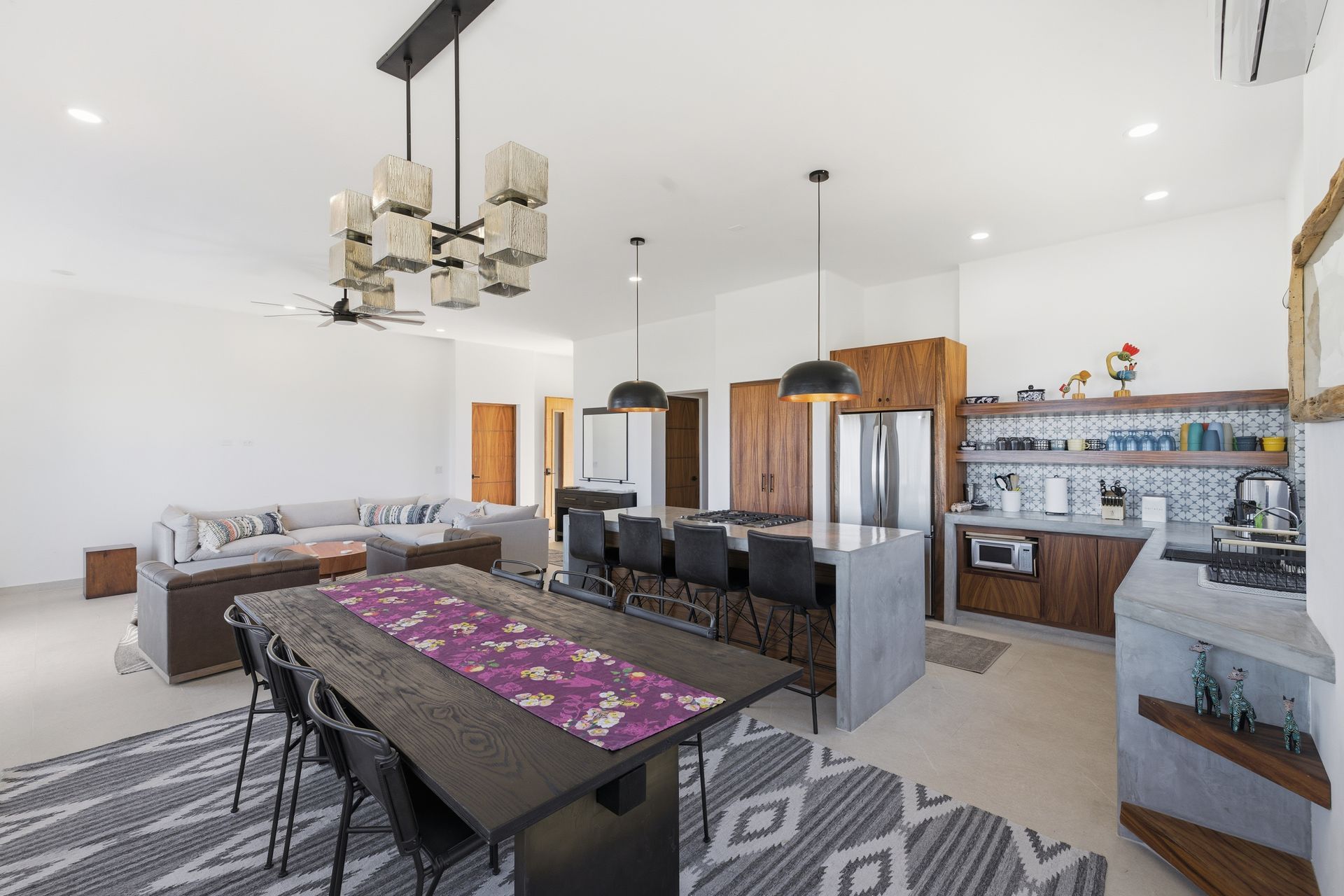 Open-concept kitchen and living area with dining table, island, and seating. White walls, wood cabinets, and gray rug.