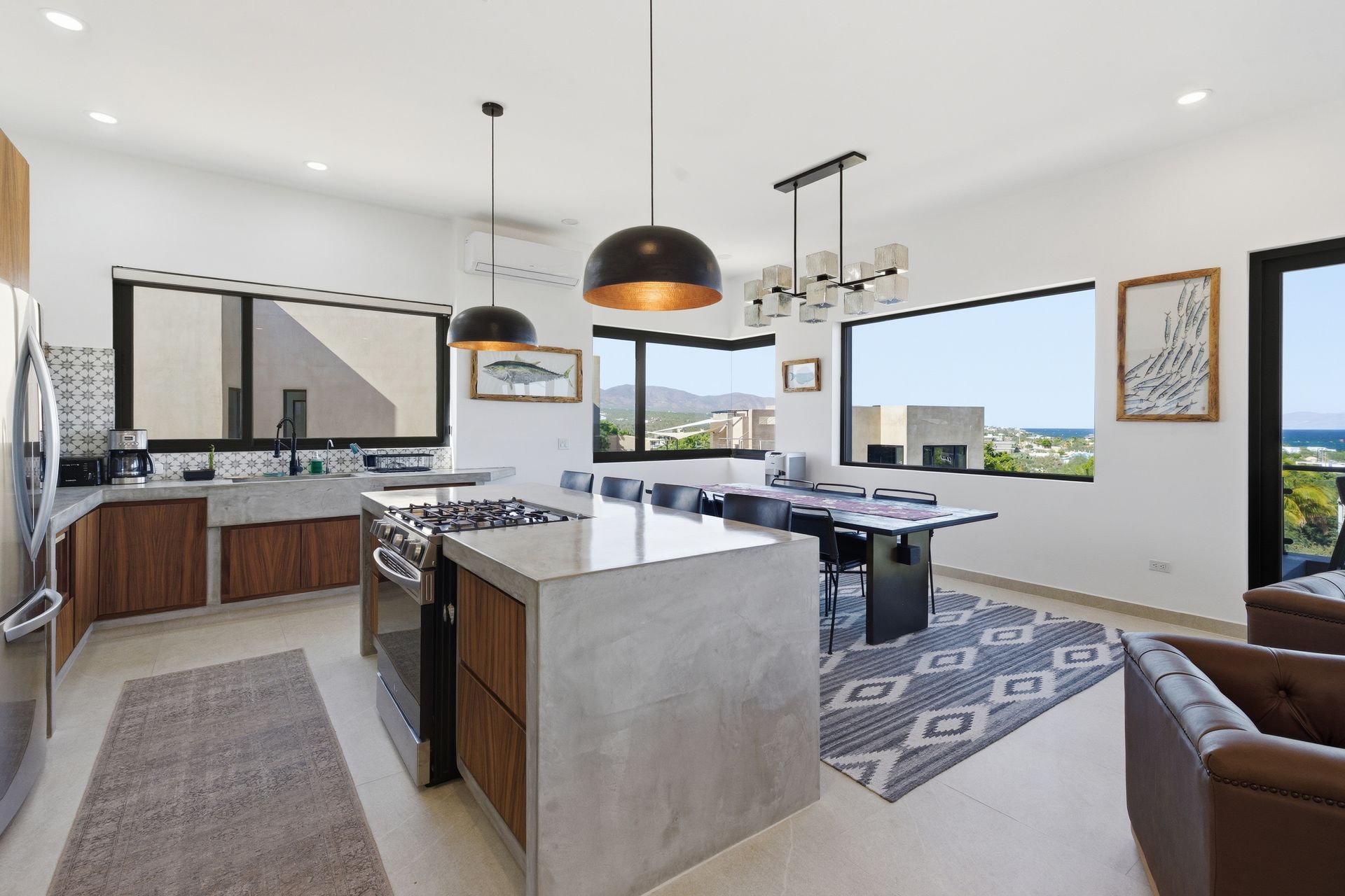 Modern kitchen with concrete island, wood cabinets, and large windows overlooking a view.