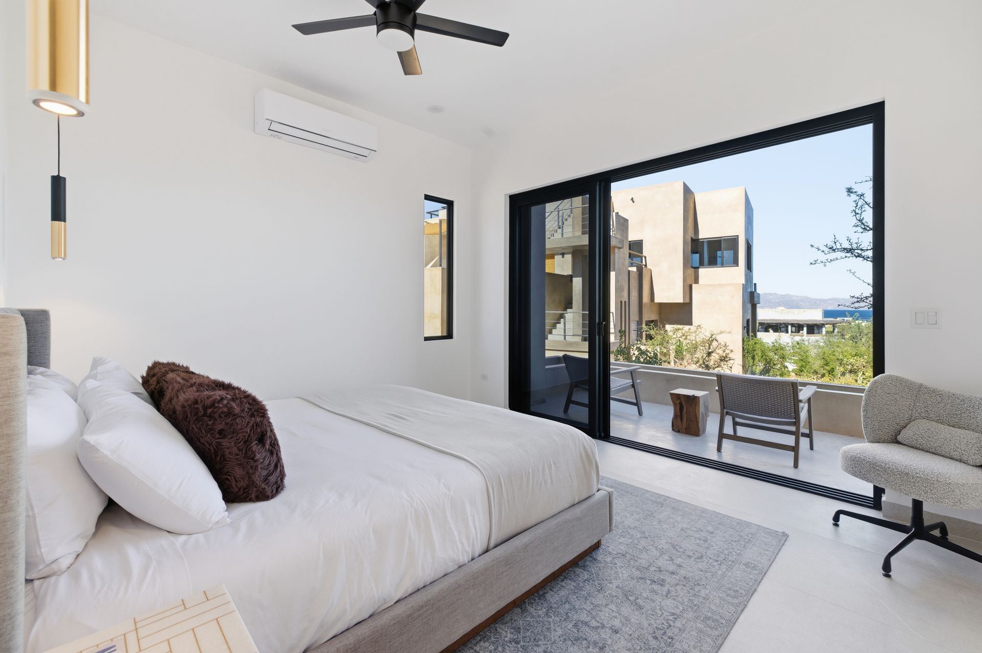 Bedroom with open door to a balcony. White walls, bed, rug, and modern furniture. Bright, sunny day.
