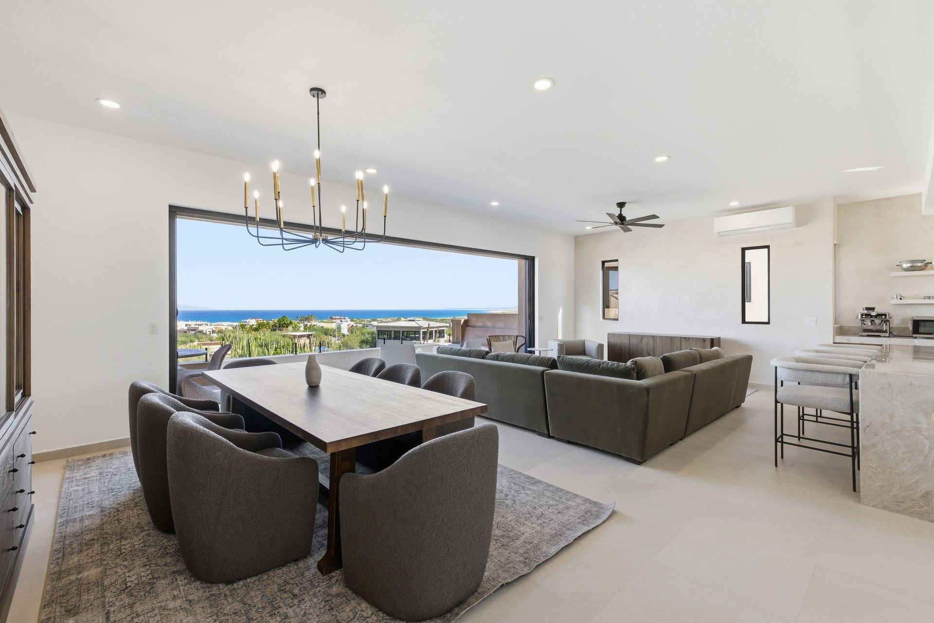 Open-concept living space with dining table, sectional sofa, and ocean view through a large window.