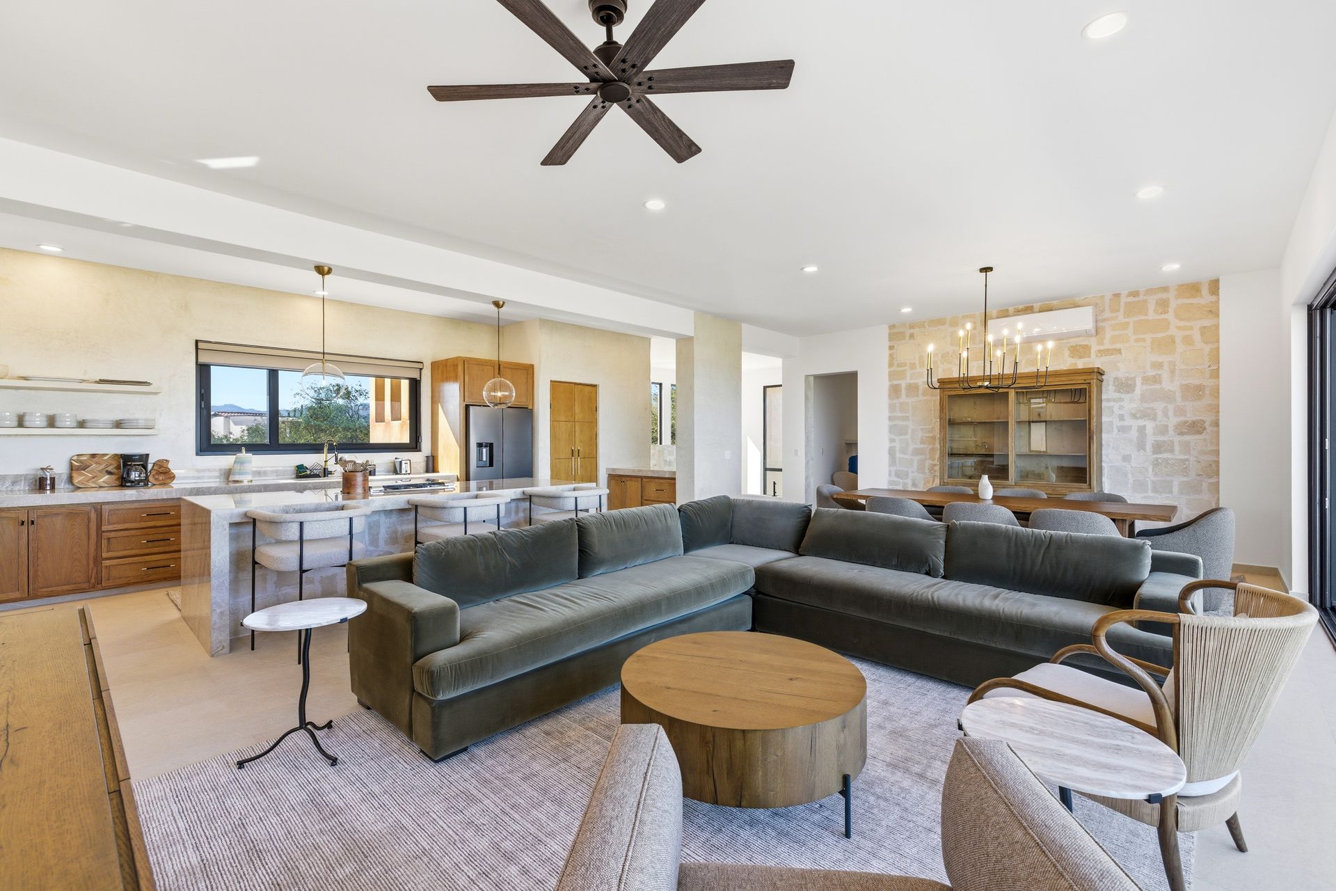 Open-concept living space with kitchen, dining, and seating areas. Green sectional sofa, wood cabinets and ceiling fan.