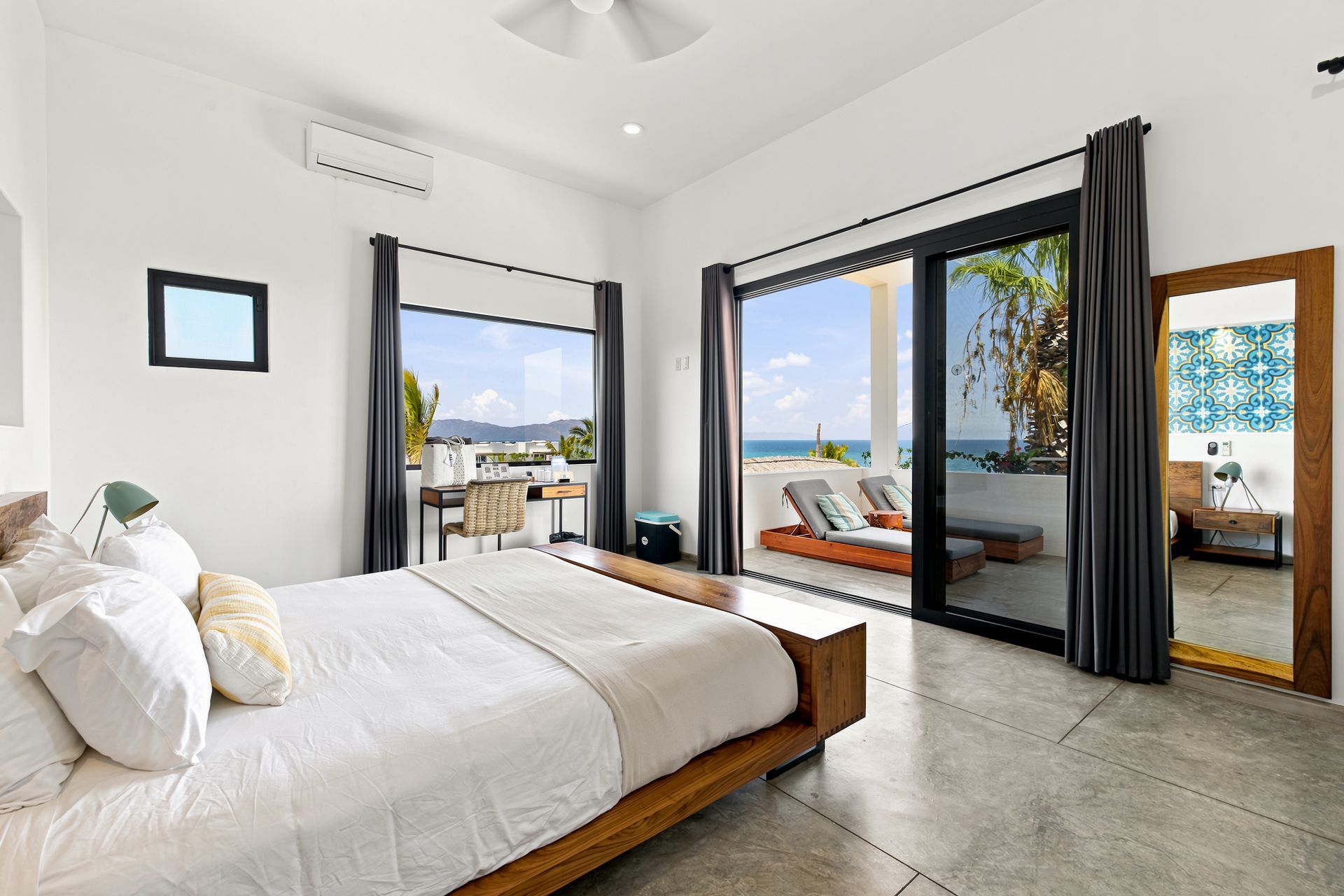 Bedroom with a bed, open glass doors, and a view of the ocean.