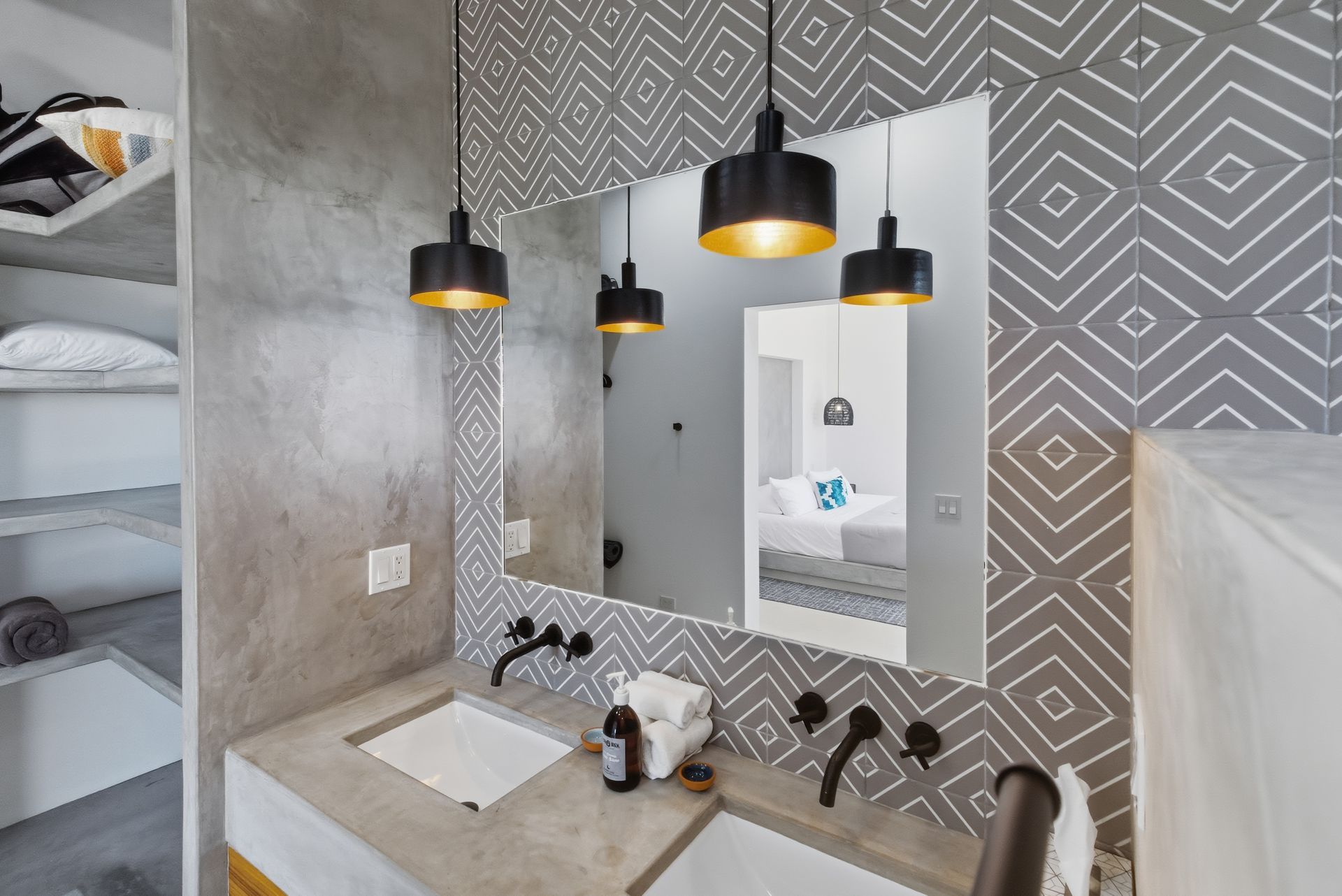 Bathroom with patterned tile, concrete countertop, black pendant lights, and large mirror.