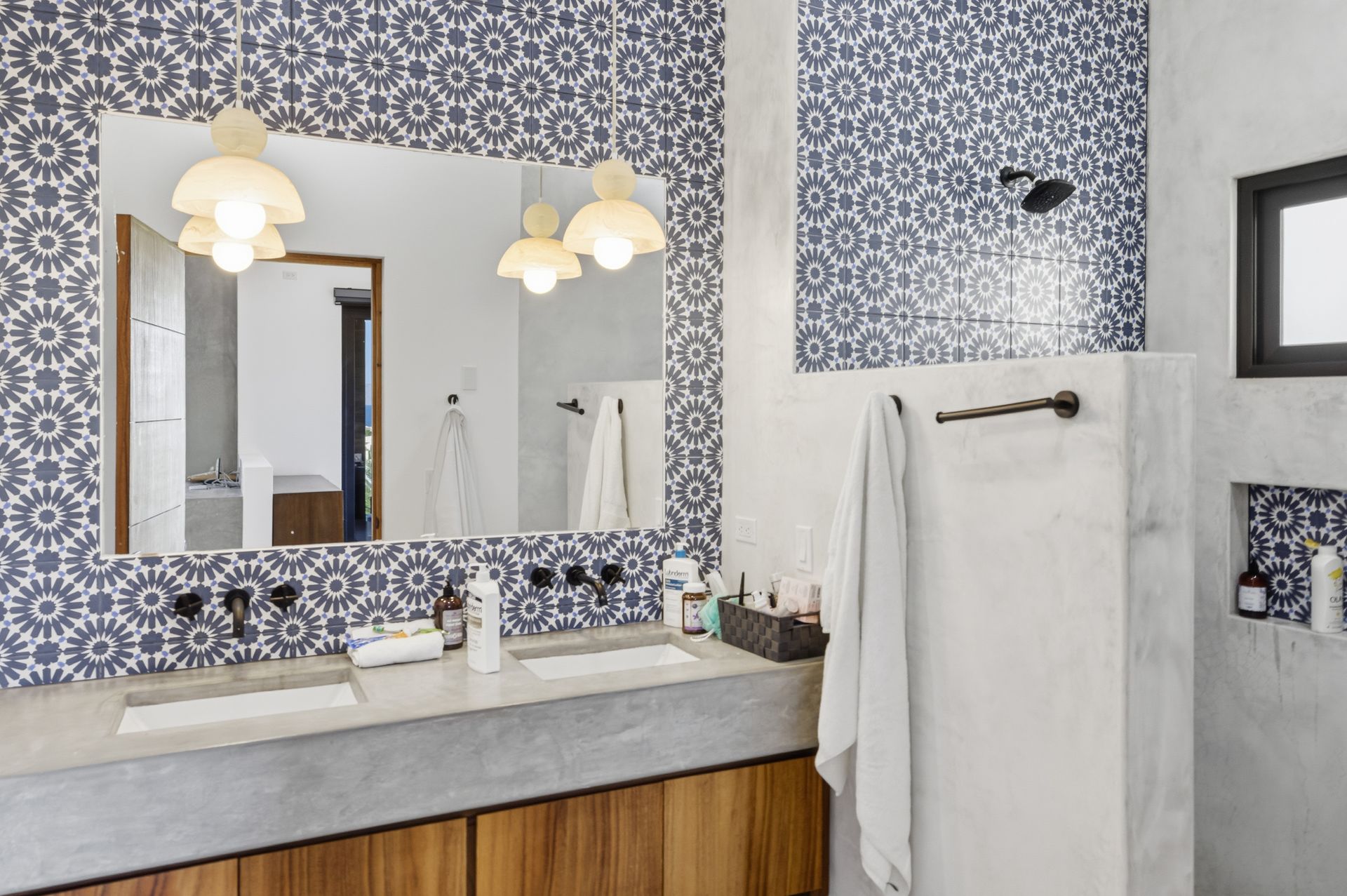 Bathroom with blue patterned tiles, concrete counter, wooden cabinets, and white pendant lights.