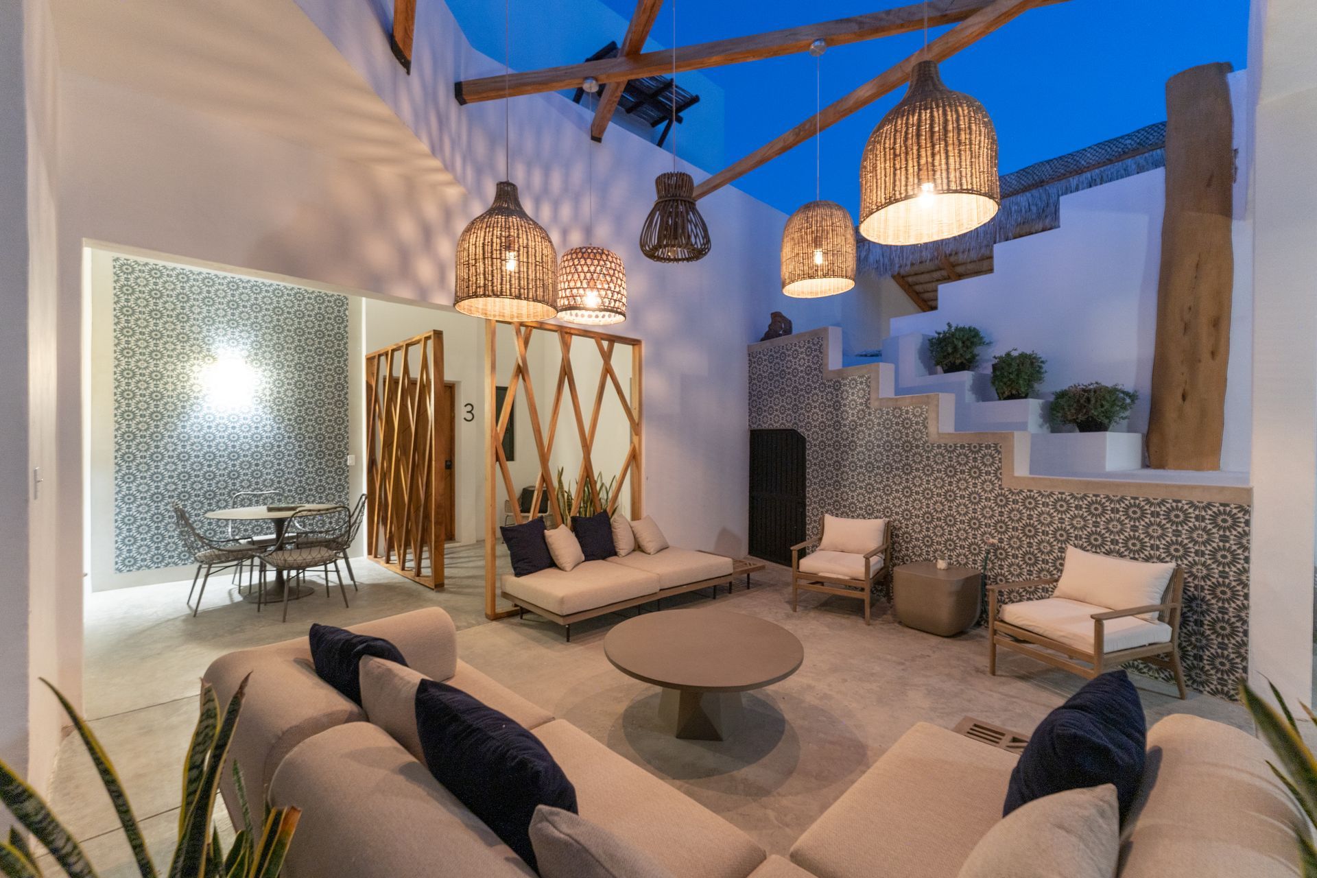 Stylish open-air living room with woven pendant lights, sofas, round table, and mosaic wall accents.