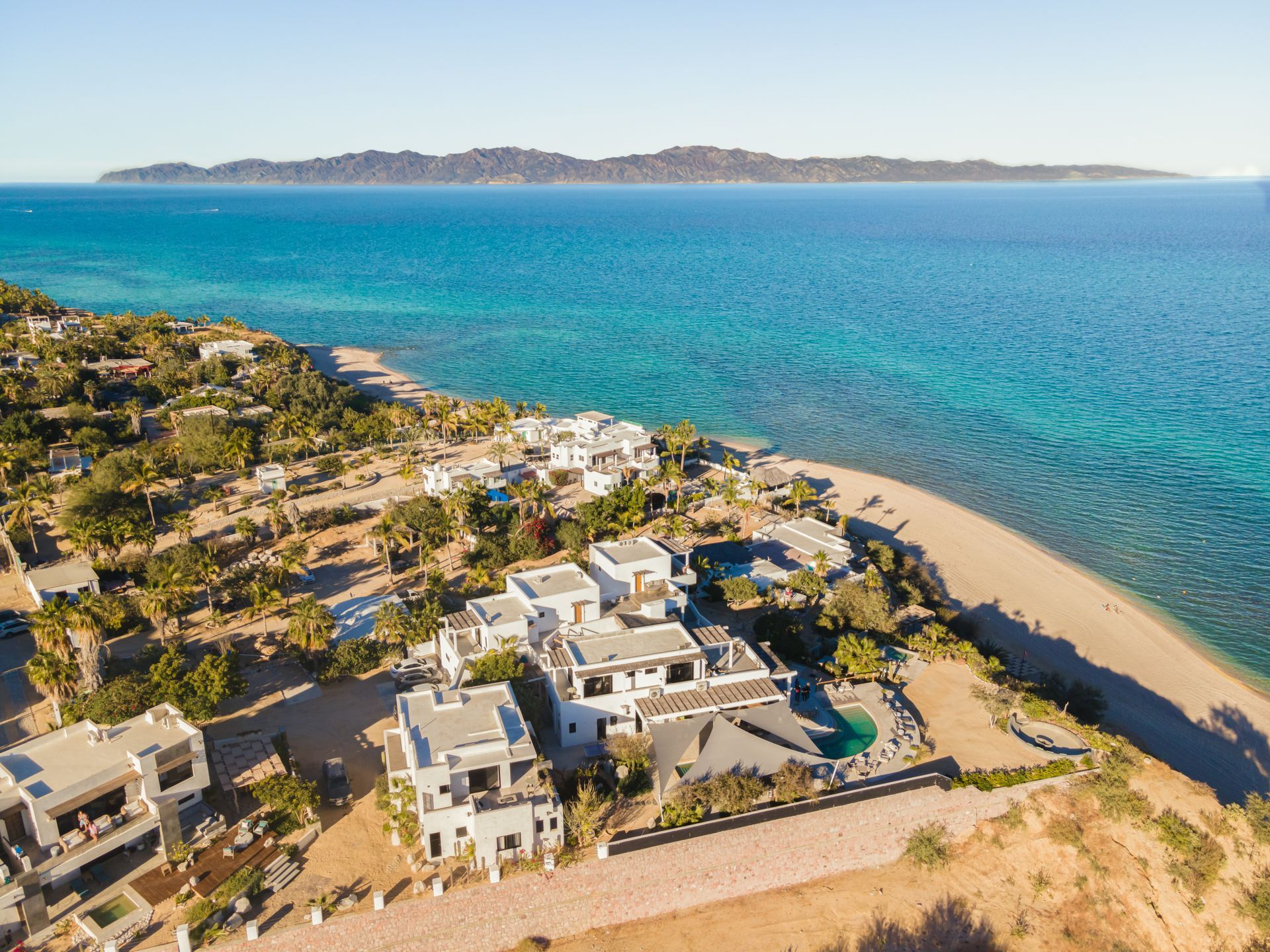 White villas on a beach, turquoise water, island in the background. Sunny day.