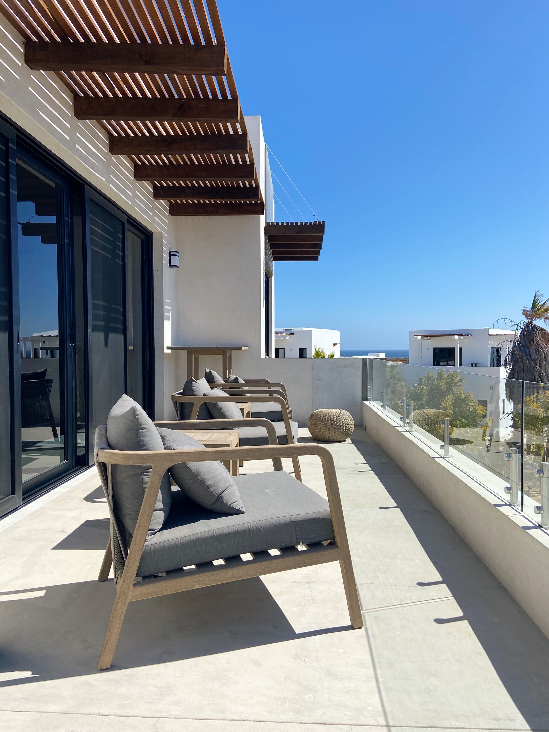 Balcony with modern gray chairs, wooden accents, and a blue sky and ocean view.