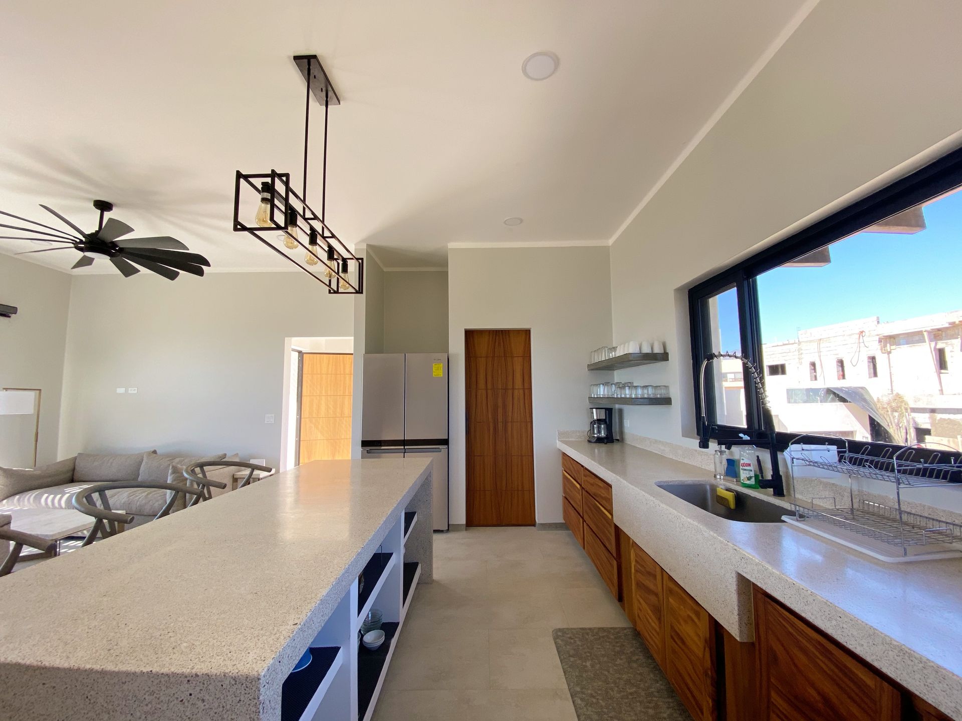 Modern kitchen with large island, wood cabinets, and large window overlooking neighborhood.