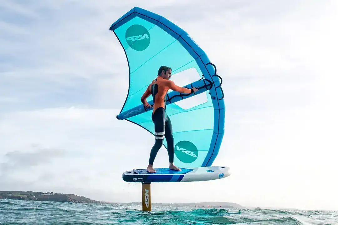 Person windsurfing, standing on hydrofoil board, blue sail, ocean setting.