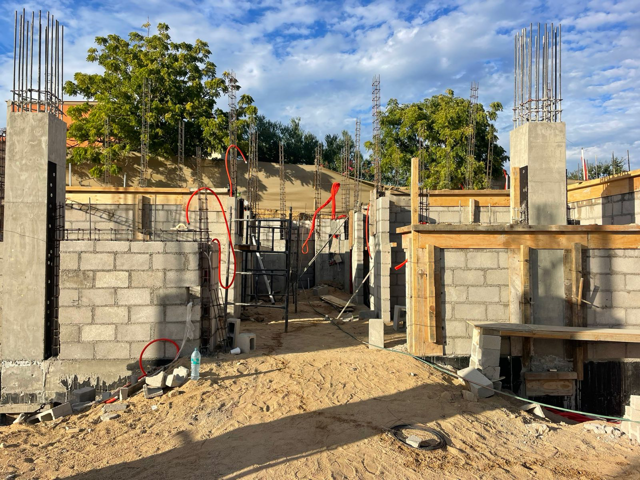 Partially built cinder block structure with rebar columns on a construction site under a blue sky