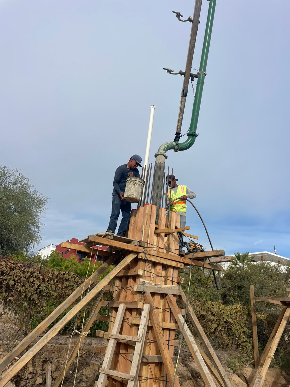 Workers on a wooden platform operating a green concrete pump at a construction site
