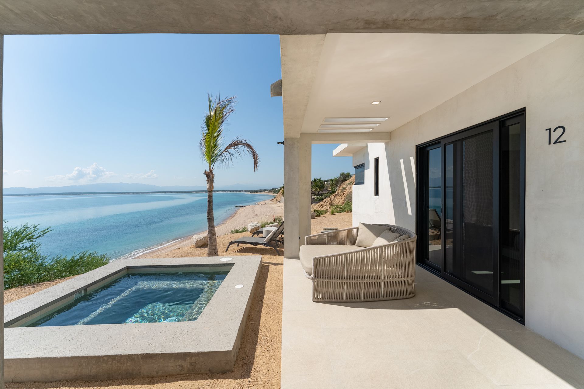 Patio with ocean view: a hot tub, seating, and beach with palm tree.