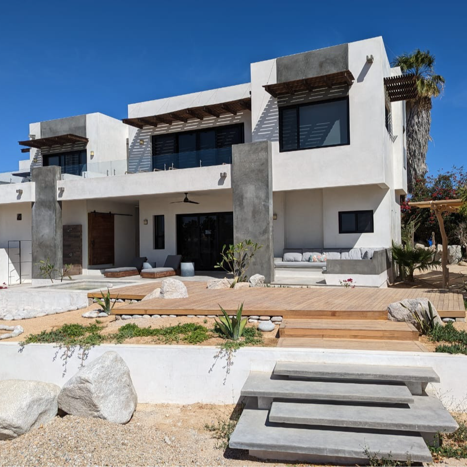 Modern, two-story white stucco house with wooden deck and concrete accents under a bright blue sky.