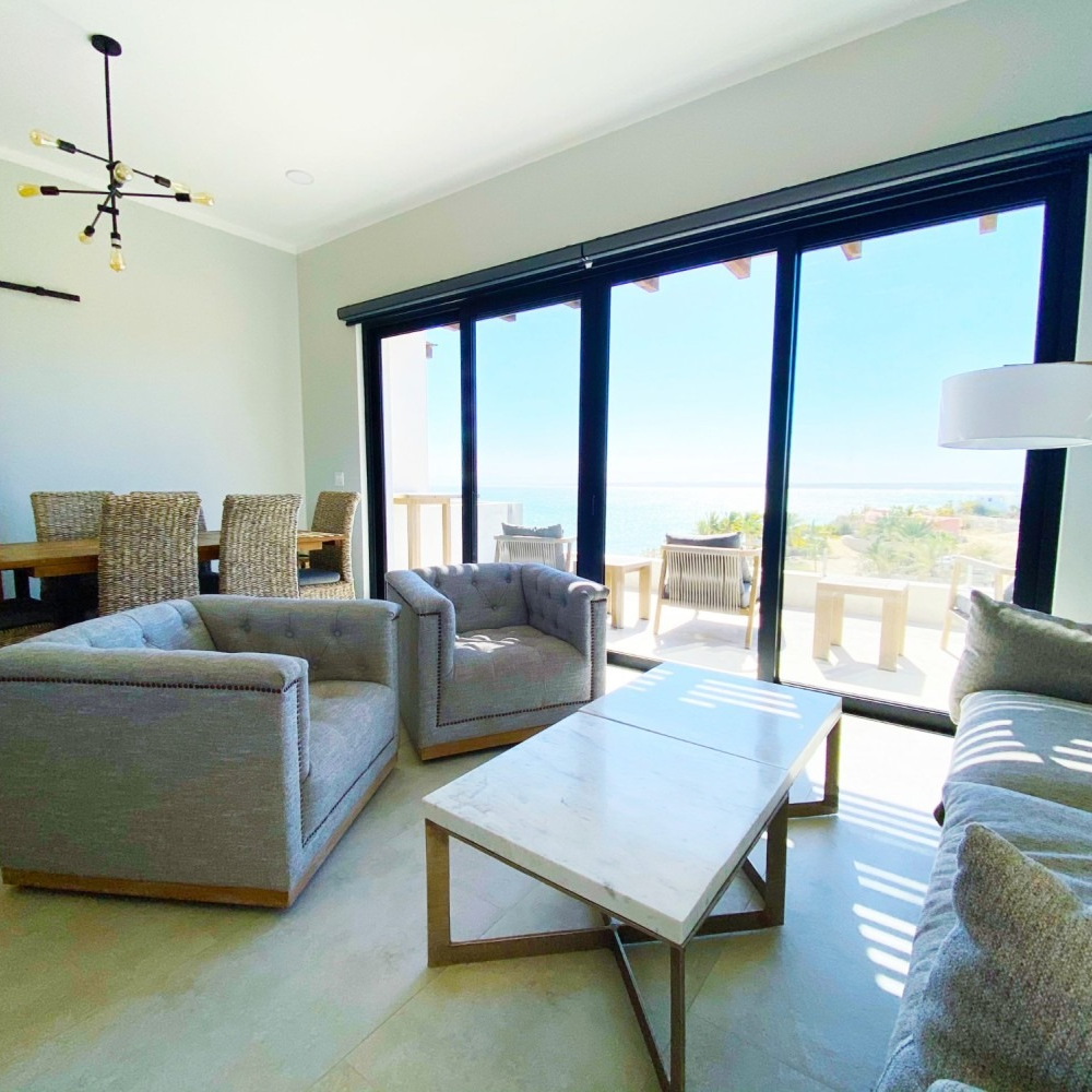Living room with gray furniture, large windows overlooking the ocean.