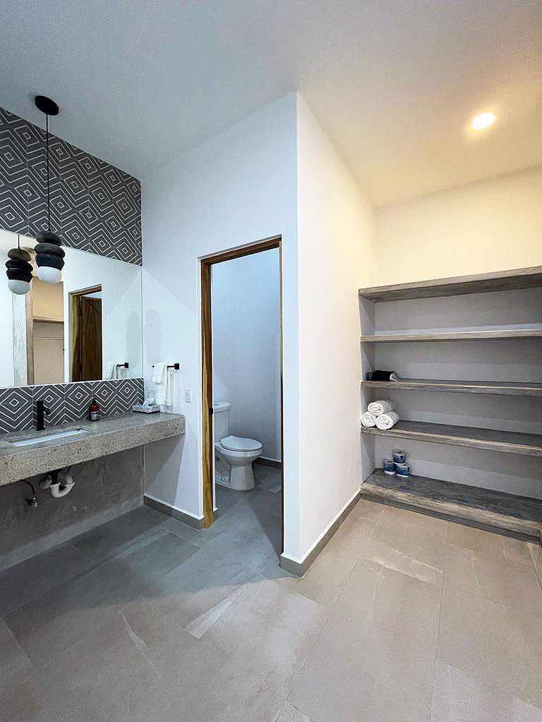 Modern bathroom with gray concrete floor, sink, shelves, and toilet.