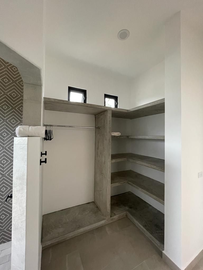 Walk-in closet with concrete shelves and a hanging rod; two small windows at the top.