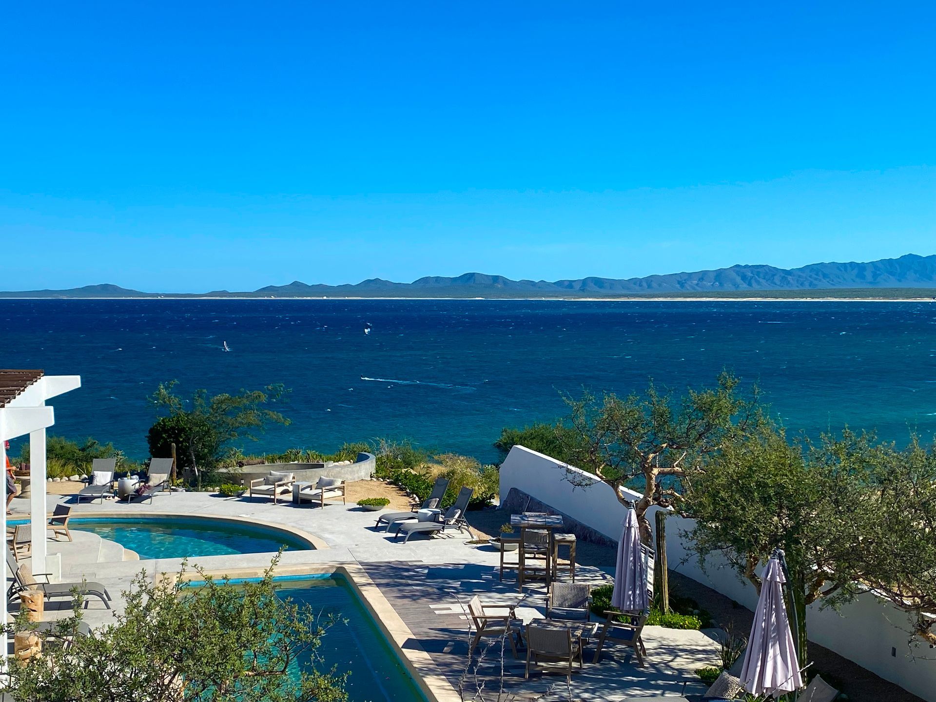 Swimming pool and patio overlooking a blue ocean under a clear sky.