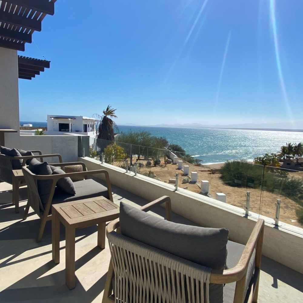 Patio with gray chairs and ocean view under a bright blue sky.