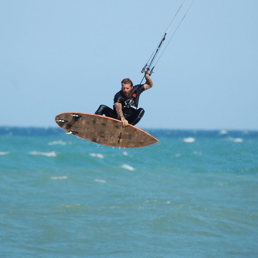 Kiteboarder in mid-air above ocean, holding lines and board. Blue sky and water.