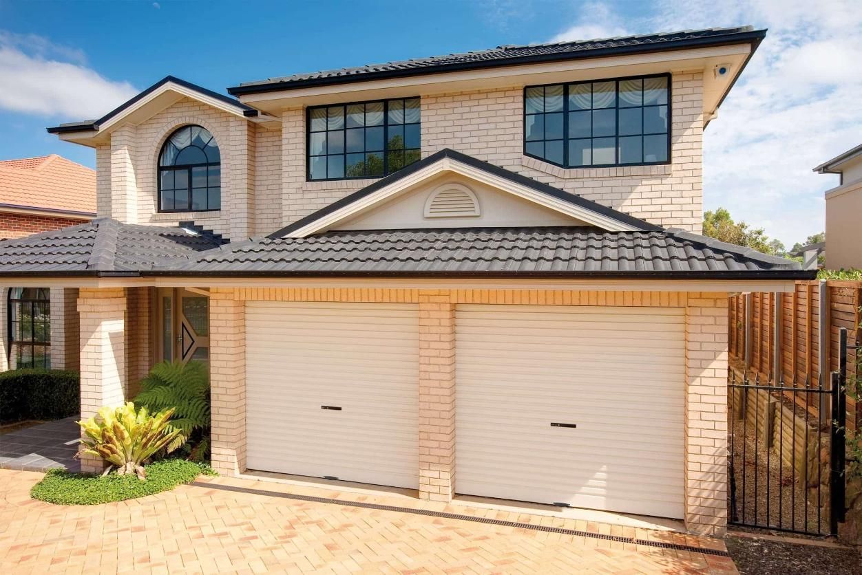 A Large Brick House With Two Garage Doors And A Black Roof — Gold Coast Door Centre In Burleigh Heads, QLD