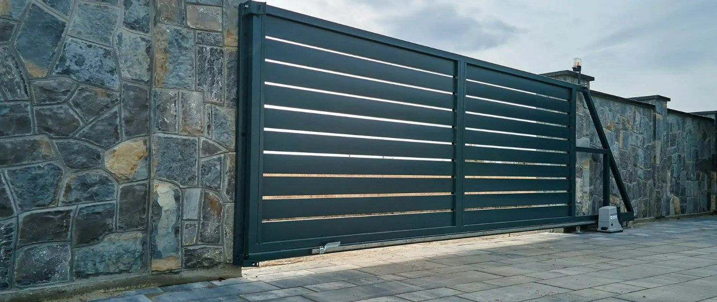 A Black Sliding Gate Is Sitting in Front of A Stone Wall — Gold Coast Door Centre In Burleigh Heads, QLD